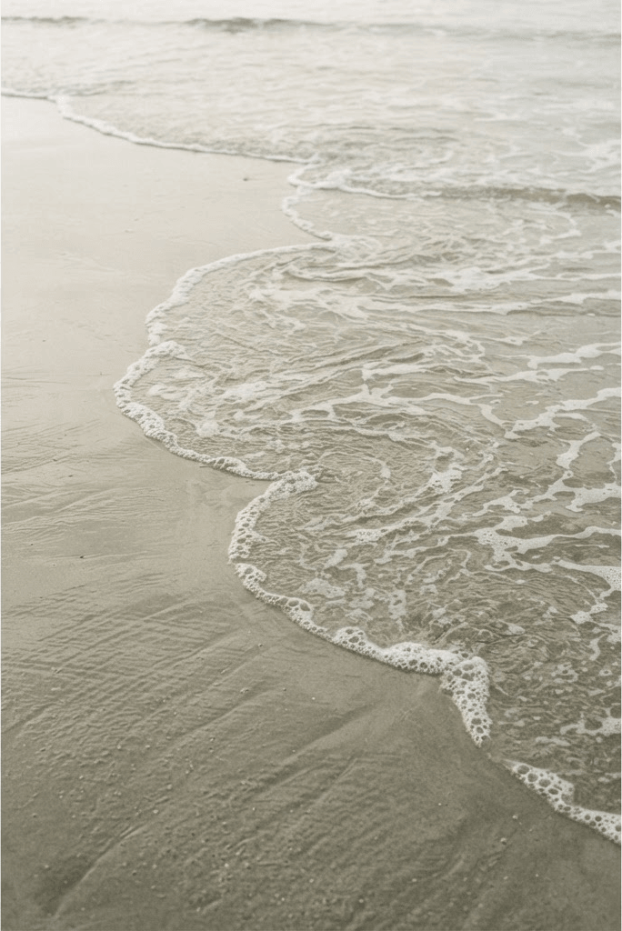 Thin sea foam dissolving over smooth wet sand